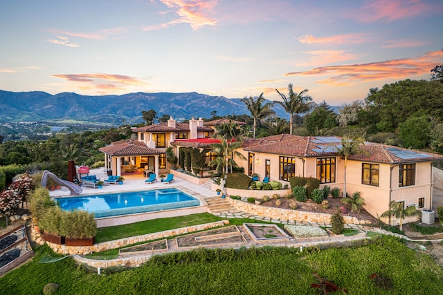 pool at dusk featuring a patio, a water slide, and a mountain view