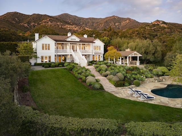 rear view of house with a lawn, a patio area, a mountain view, an outdoor pool, and stairs