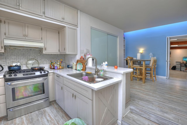 kitchen featuring sink, backsplash, kitchen peninsula, stainless steel gas range oven, and light hardwood / wood-style flooring