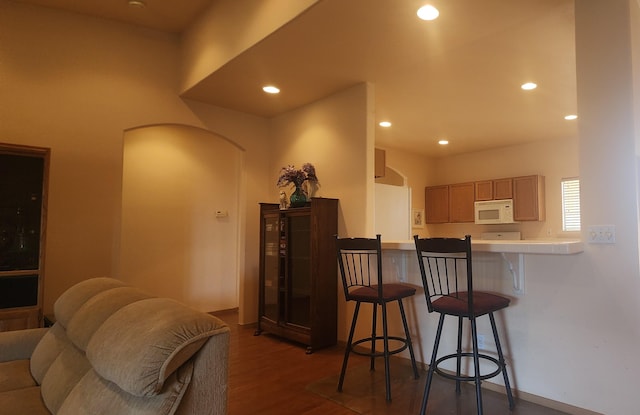 kitchen with dark wood-type flooring, white appliances, kitchen peninsula, and a breakfast bar area