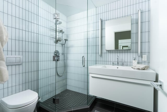 bathroom featuring walk in shower, vanity, toilet, and tile walls