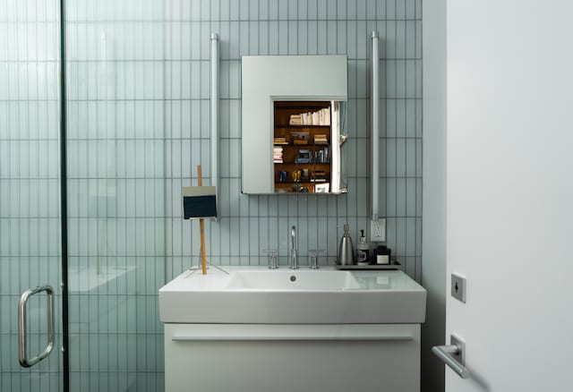 bathroom featuring vanity, a shower with door, decorative backsplash, and tile walls