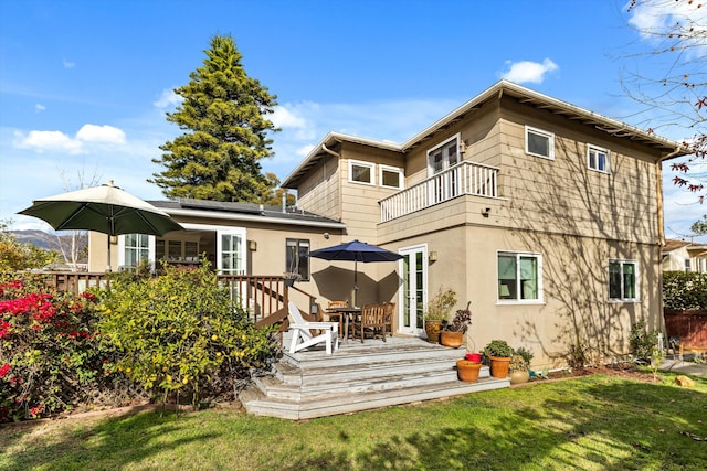 back of house featuring a wooden deck, a balcony, a yard, and solar panels