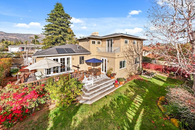 back of property featuring a lawn, a balcony, solar panels, and a deck with mountain view