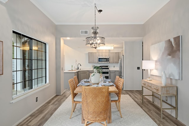 dining area featuring an inviting chandelier, ornamental molding, and light wood-type flooring