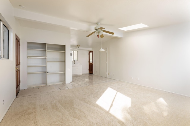 unfurnished bedroom featuring light tile patterned floors, light colored carpet, a skylight, a sink, and a ceiling fan