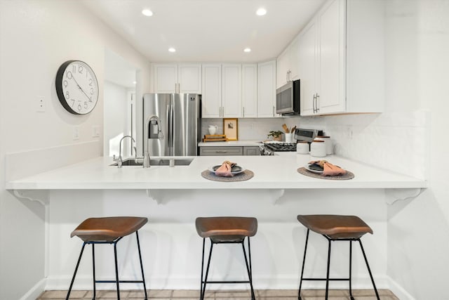 kitchen featuring a peninsula, appliances with stainless steel finishes, a sink, and tasteful backsplash