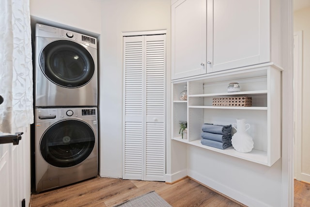 laundry area featuring light wood-type flooring, cabinets, and stacked washer / dryer