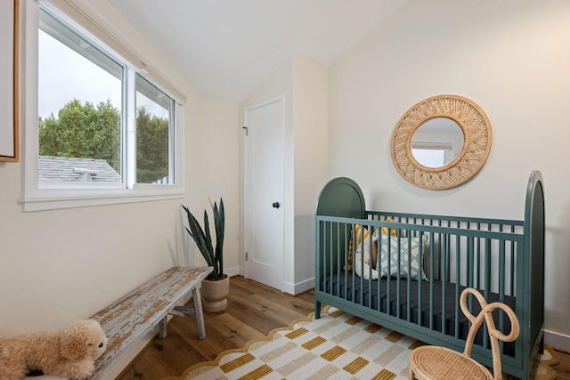 bedroom featuring lofted ceiling, wood-type flooring, and a nursery area