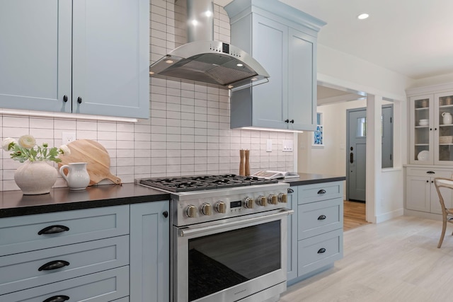 kitchen featuring white cabinetry, light wood-type flooring, high end stove, decorative backsplash, and wall chimney range hood