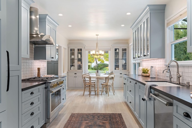 kitchen featuring pendant lighting, wall chimney range hood, sink, gray cabinets, and stainless steel appliances