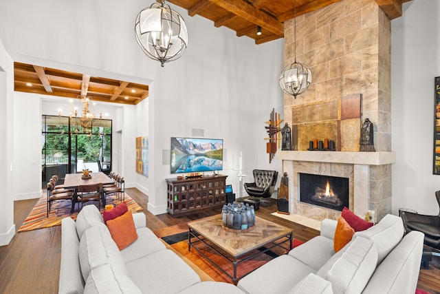 living room with a fireplace, a towering ceiling, wood-type flooring, beamed ceiling, and a chandelier