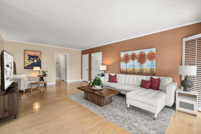 living area featuring light wood-style floors, crown molding, and baseboards