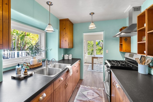 kitchen with stainless steel range with gas cooktop, hardwood / wood-style floors, pendant lighting, sink, and wall chimney range hood