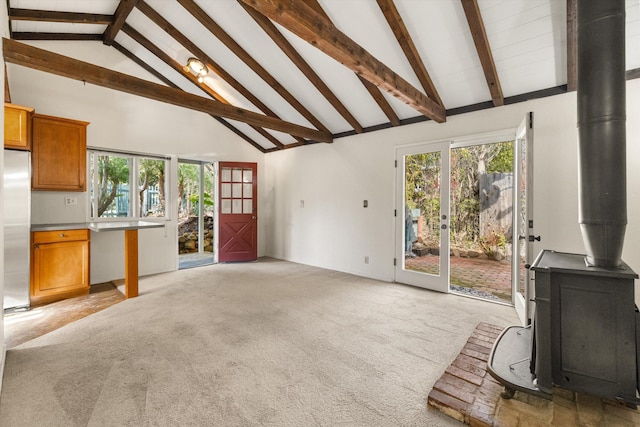 living room with light colored carpet, a healthy amount of sunlight, high vaulted ceiling, and a wood stove