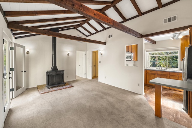 unfurnished living room with high vaulted ceiling, carpet, beamed ceiling, and a wood stove