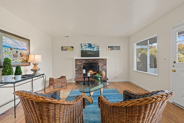 living room featuring a brick fireplace, light hardwood / wood-style flooring, and a baseboard heating unit