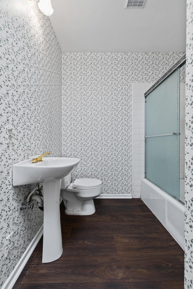 bathroom with bath / shower combo with glass door, hardwood / wood-style floors, and toilet