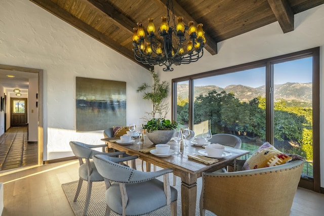 dining area featuring lofted ceiling with beams, a notable chandelier, wood ceiling, a mountain view, and light wood-type flooring