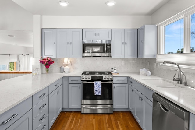 kitchen with gray cabinetry, sink, stainless steel appliances, and light stone countertops