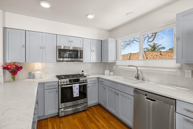 kitchen with sink, gray cabinetry, stainless steel appliances, light stone countertops, and decorative backsplash