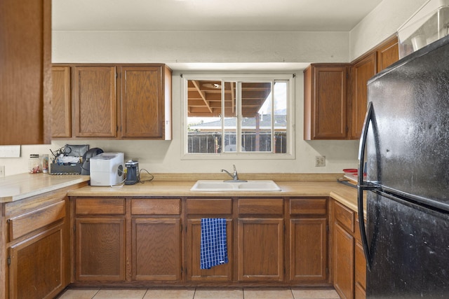 kitchen with light tile patterned flooring, sink, and black refrigerator