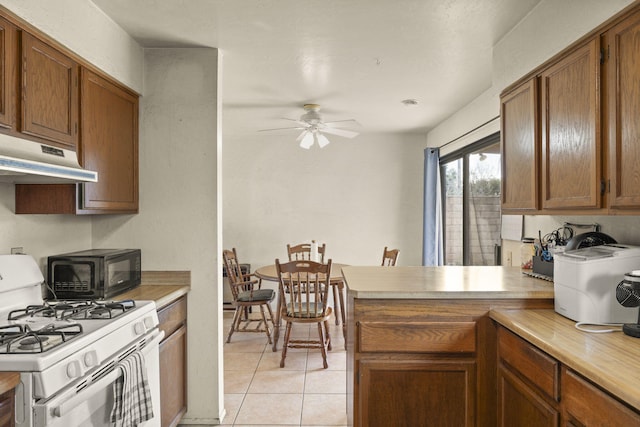 kitchen featuring ceiling fan, light tile patterned flooring, kitchen peninsula, and white gas range