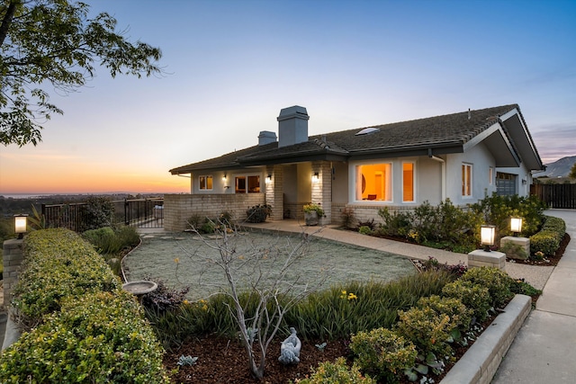 back of house at dusk featuring a chimney, fence, and stucco siding