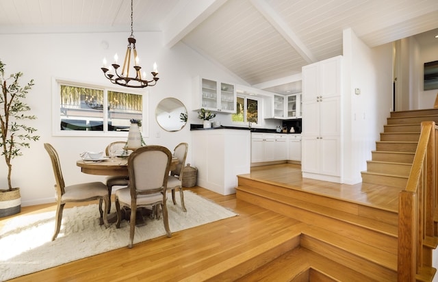 dining space with vaulted ceiling with beams, a chandelier, and light wood-type flooring