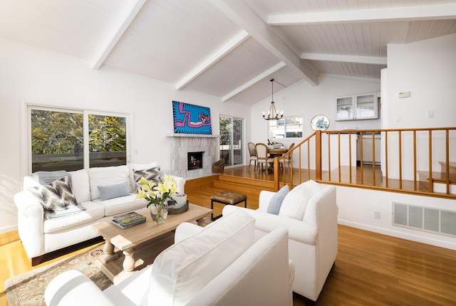 living room featuring visible vents, a tiled fireplace, lofted ceiling with beams, stairway, and a chandelier