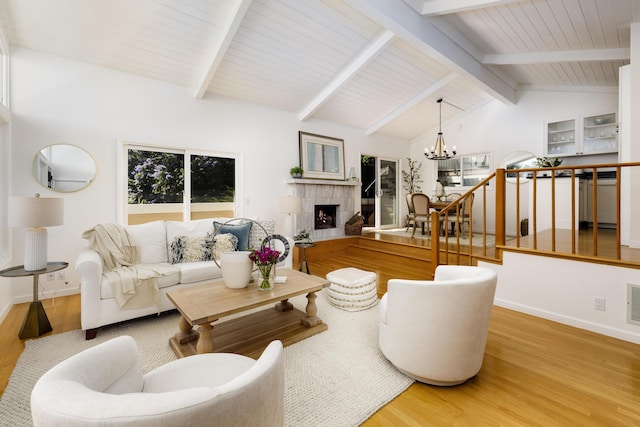 living room featuring a notable chandelier, vaulted ceiling with beams, visible vents, light wood-type flooring, and a warm lit fireplace