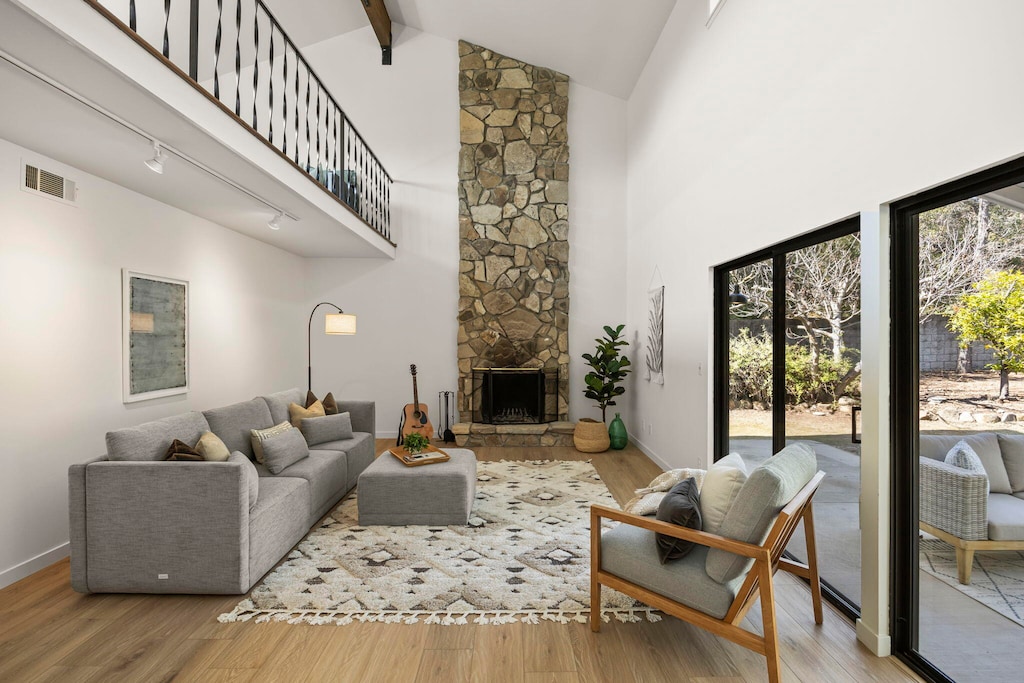 living room featuring high vaulted ceiling, a stone fireplace, light hardwood / wood-style floors, and beam ceiling