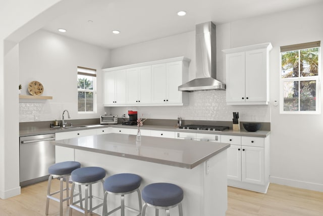 kitchen featuring wall chimney exhaust hood, sink, a center island, stainless steel appliances, and white cabinets