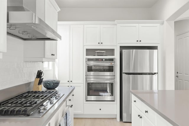 kitchen featuring wall chimney range hood, stainless steel appliances, tasteful backsplash, light hardwood / wood-style floors, and white cabinets