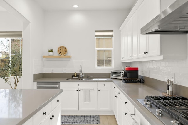 kitchen with appliances with stainless steel finishes, white cabinetry, sink, decorative backsplash, and wall chimney range hood