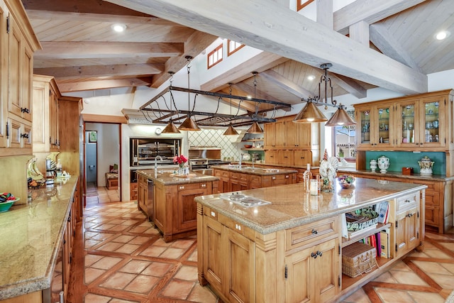 kitchen featuring pendant lighting, backsplash, vaulted ceiling with beams, light stone counters, and an island with sink