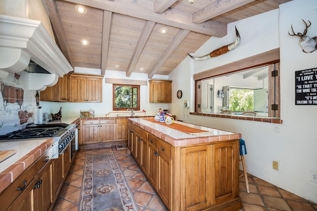 kitchen with stainless steel gas cooktop, a center island, lofted ceiling with beams, wooden ceiling, and tile counters