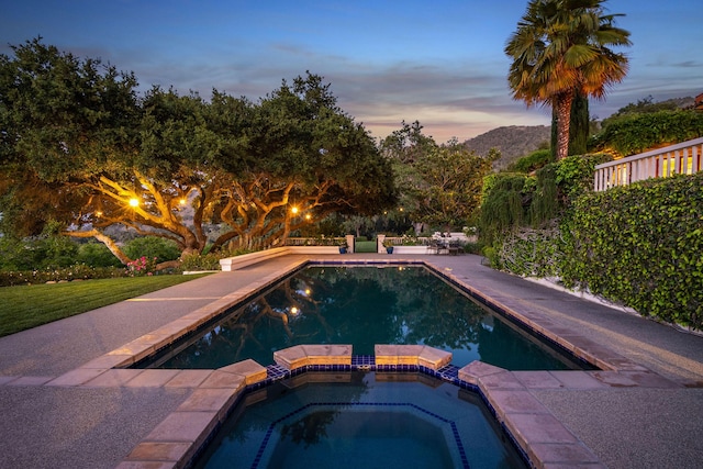 pool at dusk featuring a mountain view, a patio area, and an in ground hot tub