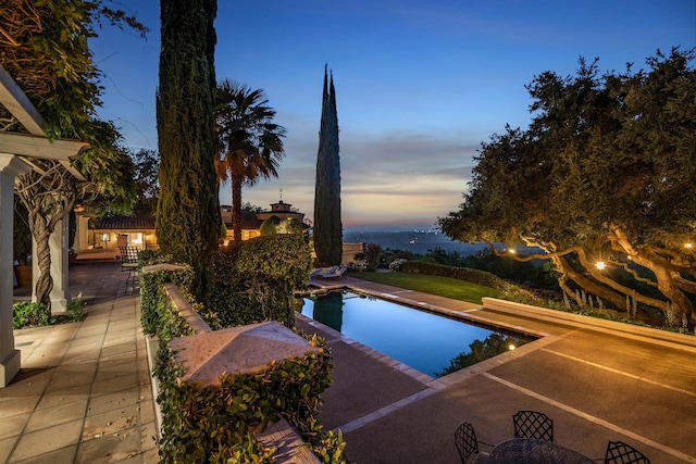 pool at dusk with a patio area