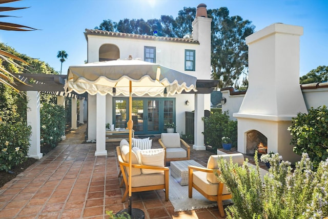 rear view of property with french doors, a patio, and an outdoor living space with a fireplace