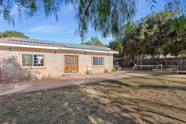 rear view of property with a yard, a trampoline, and a patio area