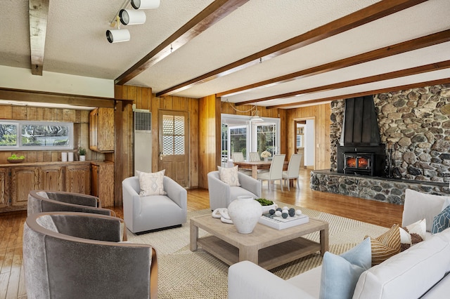 2385 Janin Pl, Solvang, CA 93463 - living room featuring wooden walls, beamed ceiling, a wood stove, light wood-type flooring, and a textured ceiling