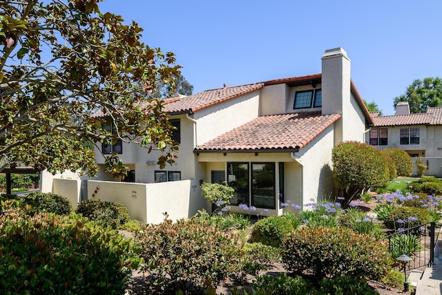 back of property with a chimney, fence, a tiled roof, and stucco siding