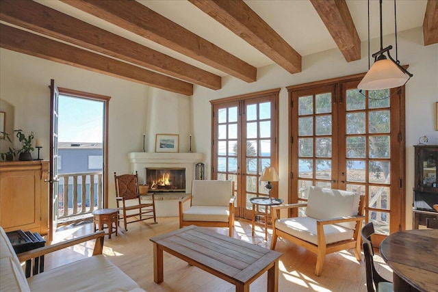 living area featuring a water view, beamed ceiling, light hardwood / wood-style floors, a fireplace, and french doors