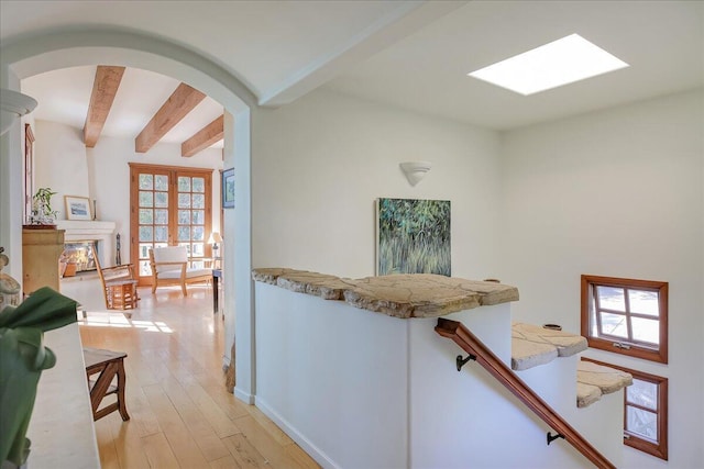 hall with a skylight, light hardwood / wood-style flooring, and beam ceiling