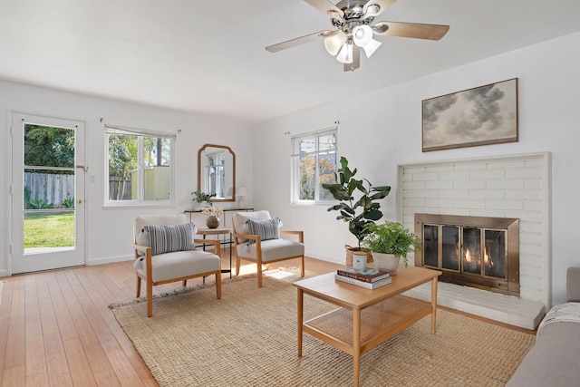 living area featuring baseboards, a brick fireplace, plenty of natural light, and light wood-style floors