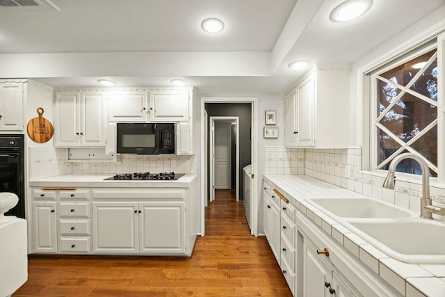 kitchen with white cabinets, a sink, light wood-style floors, decorative backsplash, and black appliances