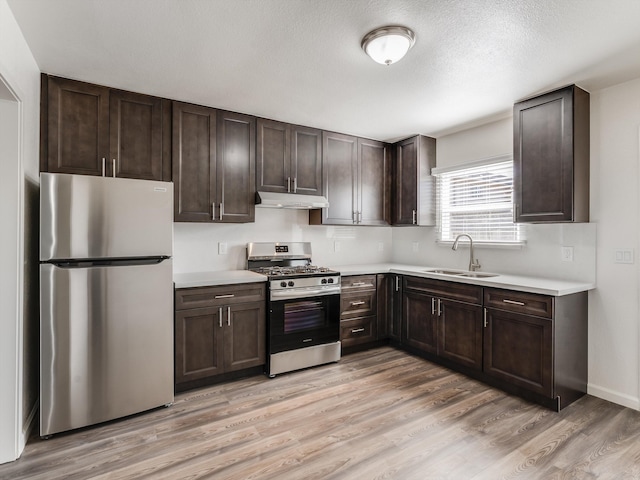 kitchen featuring appliances with stainless steel finishes, sink, light wood-type flooring, a textured ceiling, and dark brown cabinets