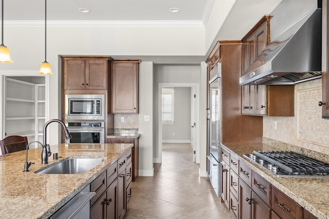 kitchen featuring stainless steel appliances, decorative light fixtures, sink, light stone counters, and wall chimney range hood