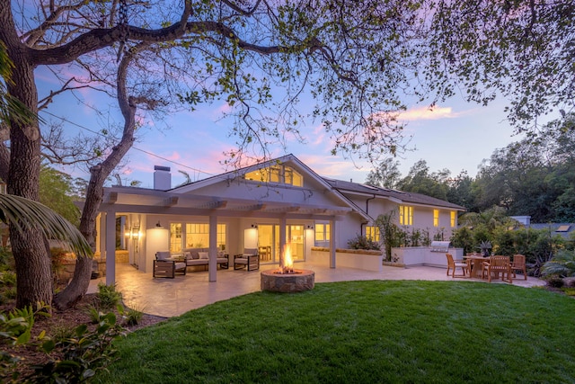 rear view of house featuring a patio area, an outdoor living space with a fire pit, a lawn, and stucco siding